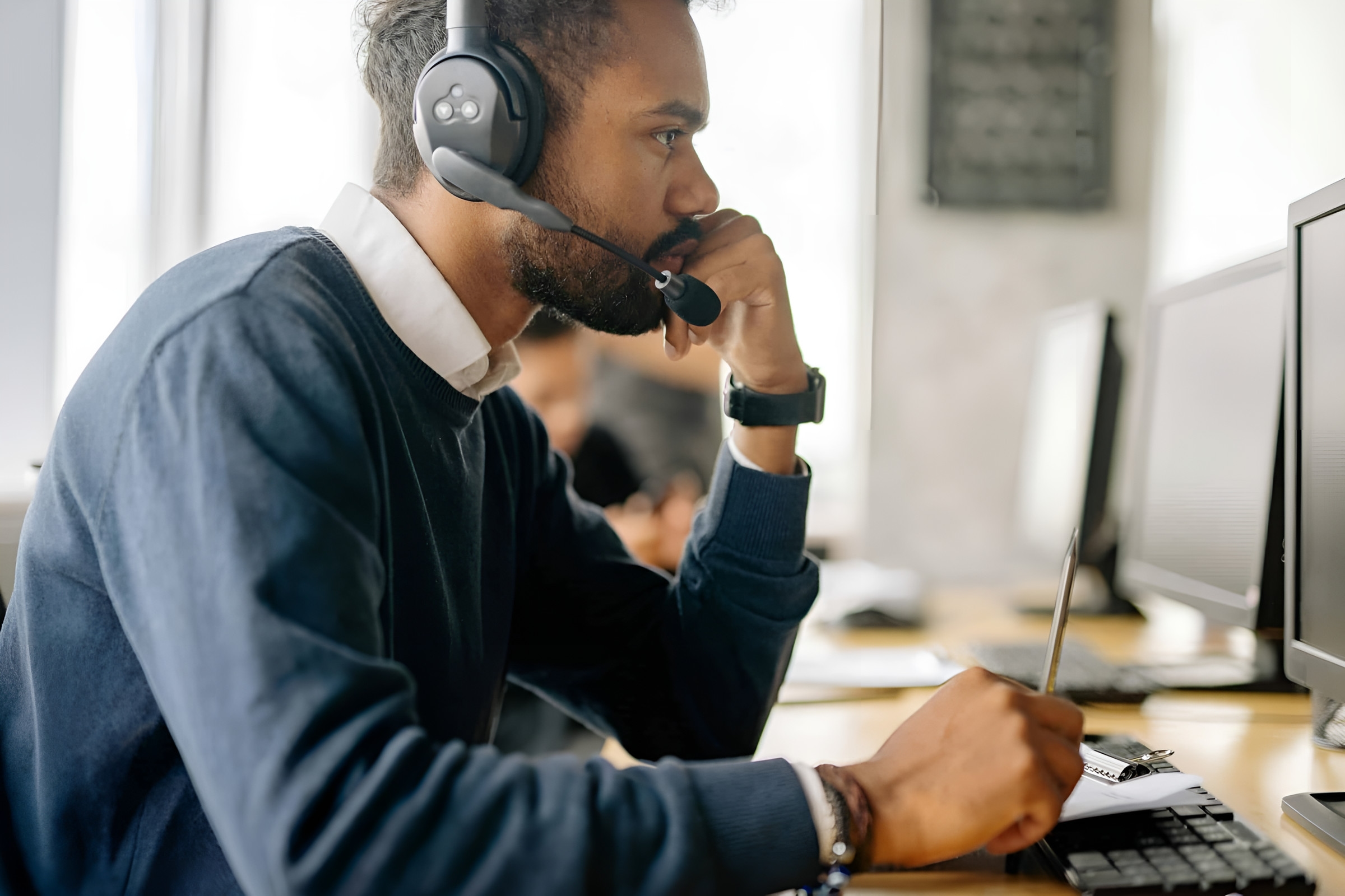 A person with a headset taking notes at a computer desk